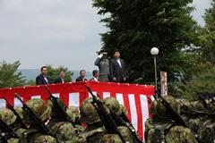 紅白のマントに囲われたステージ上に立っている男性に対して、敬礼をしている自衛官の写真