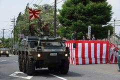 装甲車から日章旗を持っている自衛官とステージ上に向かって敬礼をしている自衛官の写真