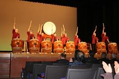ステージ上で赤い法被姿の人たちが並んで和太鼓を演奏している写真