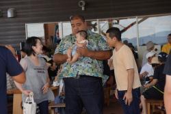 元横綱 武蔵丸が赤ちゃんを抱っこし、男性と女性が赤ちゃんに微笑みかけている写真