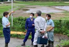 市長が作業服を着た3名の関係者に田んぼの方を指さし話をしている写真