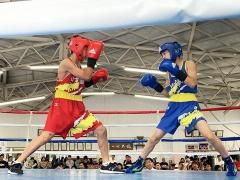 ボクシングのリング上で右側に青色のユニフォーム姿の選手、左側に赤色のユニフォーム姿の選手が立ち、向かい合っている写真