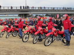 赤いジャケットと赤いヘルメットをした団員達が、赤いバイクの横に起立して並んでいる写真