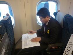 新幹線の車内に座り、書類を見ている市長の写真