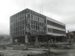 建物の窓が割れ、あたりにがれきと、ショベルカーが写る白黒写真
