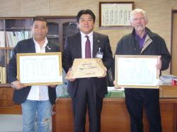 額に入った賞状を持つゲーリー・ブコブニック氏と、冨田氏の間に立つ市長の記念写真