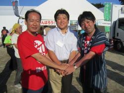 市長と赤いシャツを着た男性2名が手を重ねている写真