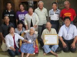 高齢の女性と、その横で額に入った賞状を持つ男性、市長や、家族の記念写真