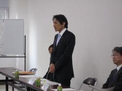 松野内閣官房副長官が起立し話をしている写真