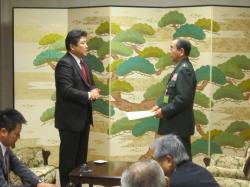 松の木が描かれた屏風の前でえびの市長と軍服姿の男性が向かい合わせに立っている写真