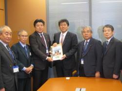 中央に要望書を手に持った古川議員とえびの市長、両脇に4名のスーツを着た男性が並んでいる写真
