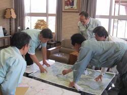 低いテーブルに広げられた地図を指さしながら東国原知事に説明している市長や関係者の写真