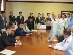 向かい合って着席している関係者の中で、中腰の姿勢で意見を述べる東国原知事の写真