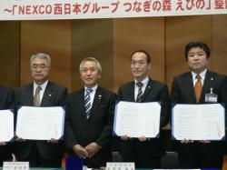 協定調印式にて、協定書を持つ市長、東国原知事、男性が並ぶ記念写真