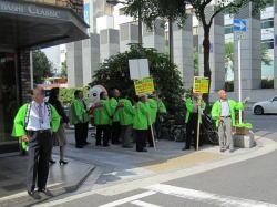 緑の法被を着た関係者が、ポールをもって歩道に立っている写真
