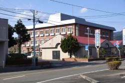 道路に面した えびの市立病院の茶色い建物と右横の赤屋根の建物を道路側から写した写真